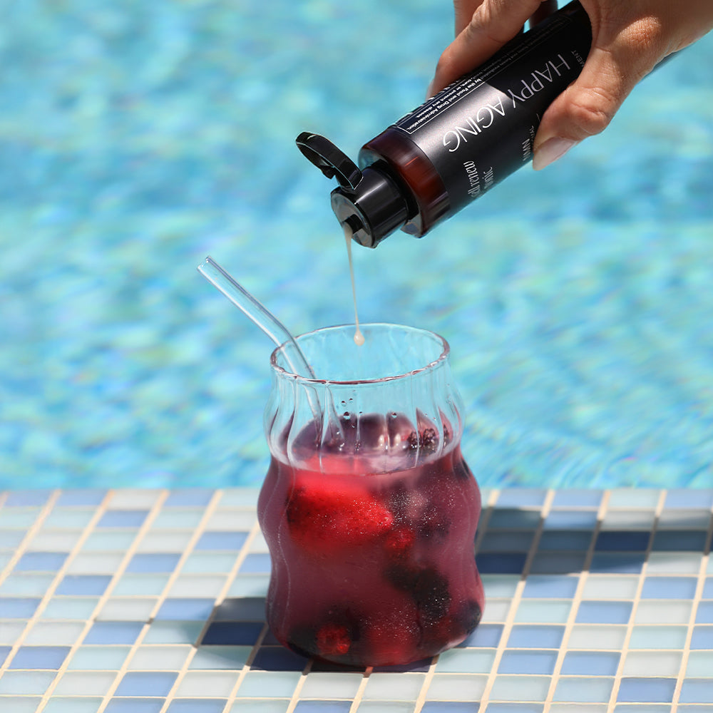 Person pouring a red liquid from a bottle into a glass by a pool.