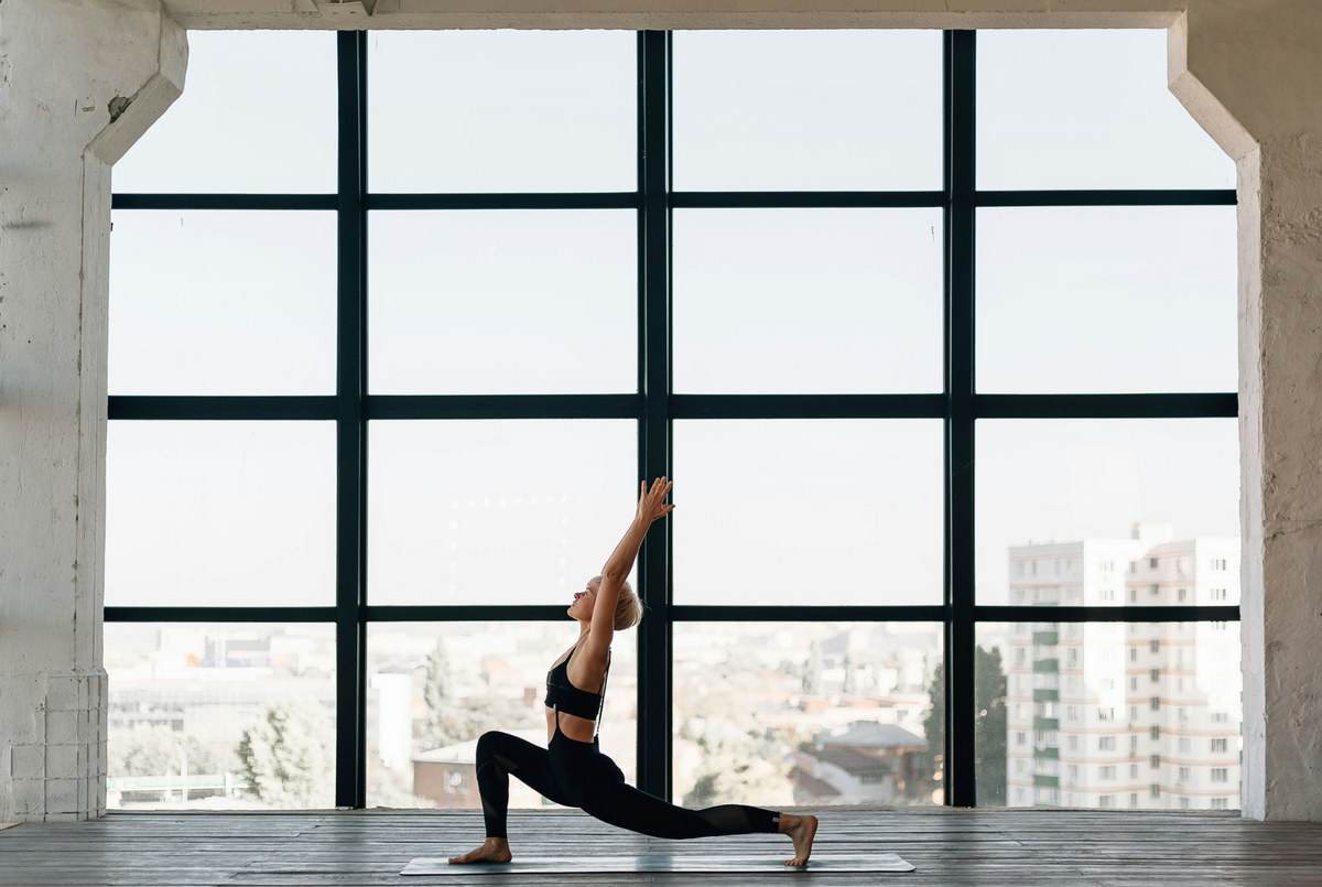 Woman practing yoga balancing her body in front of a big window with a sky view