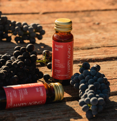 Two bottles of 'Happy Aging' supplement with grapes on a wooden surface