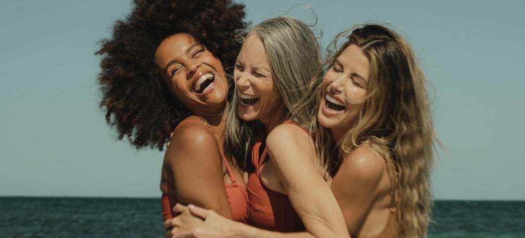 Three women laughing together on the beach